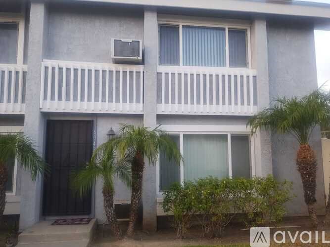 A two-story building with a balcony and palm trees in front.