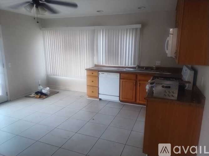 A room with a fan, a window with blinds, a white washing machine, and a wooden cabinet.