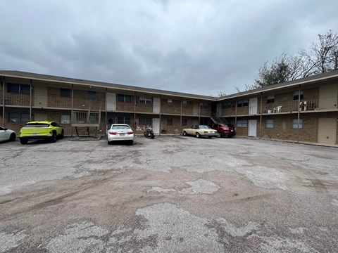 A parking lot with cars and a motorcycle in front of apartment buildings.