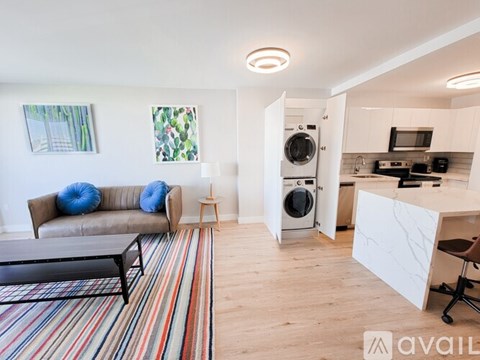 A living room with a couch, a striped rug, and a kitchen area in the background.