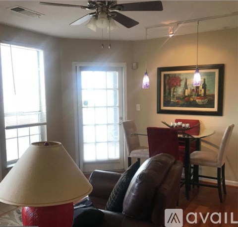 A living room with a brown leather couch, a red lamp, a dining table with chairs, and a painting on the wall.