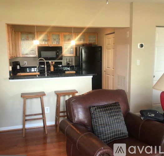 A brown leather couch with a checkered pillow sits in a kitchen with a black refrigerator and a black countertop.