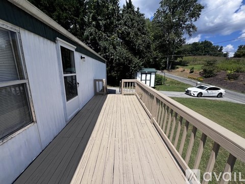 A white house with a wooden deck and a car parked in the driveway.