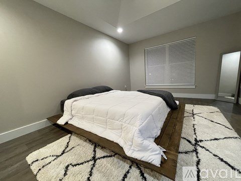 A bedroom with a white bedspread and a black and white rug.