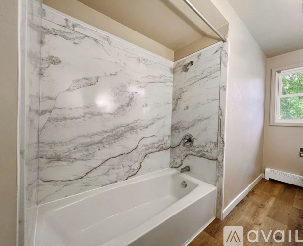 A bathroom with a marble patterned tub and a window.