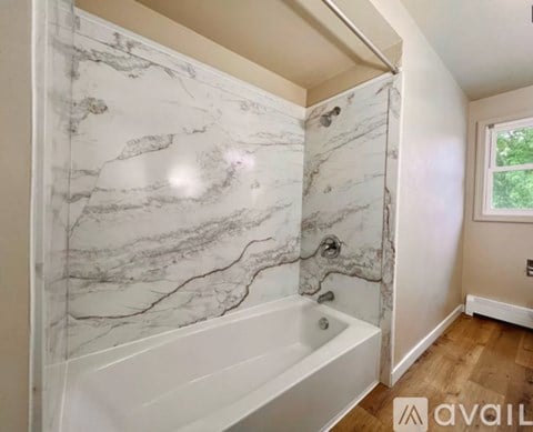 A bathroom with a marble patterned tub and a window.