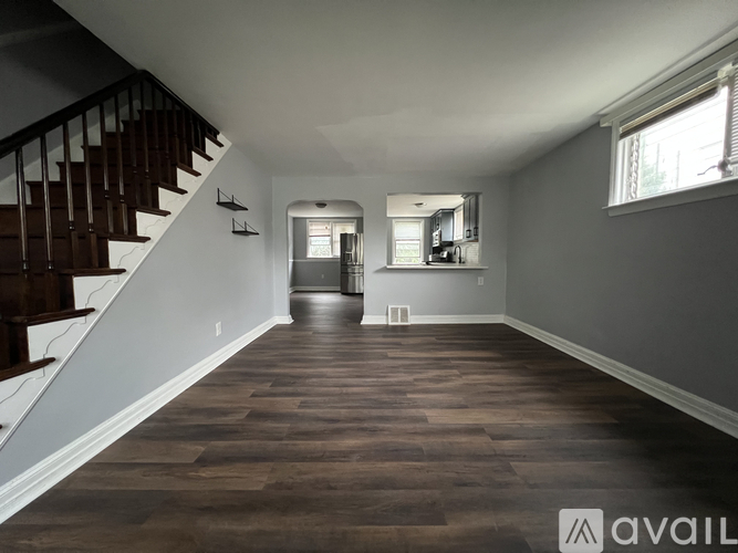 A spacious room with wooden floors and a staircase on the left side.