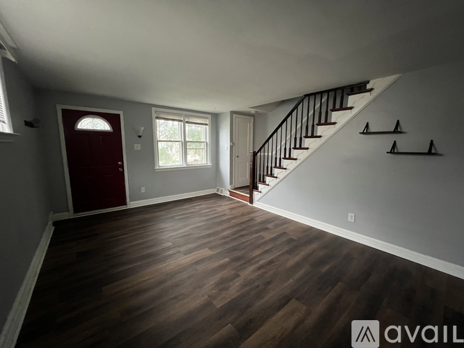A room with a red door, wooden floors, and a staircase with black railings.