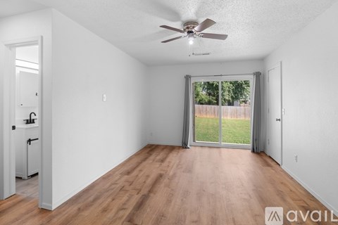 A room with a ceiling fan and sliding glass doors leading to a backyard.