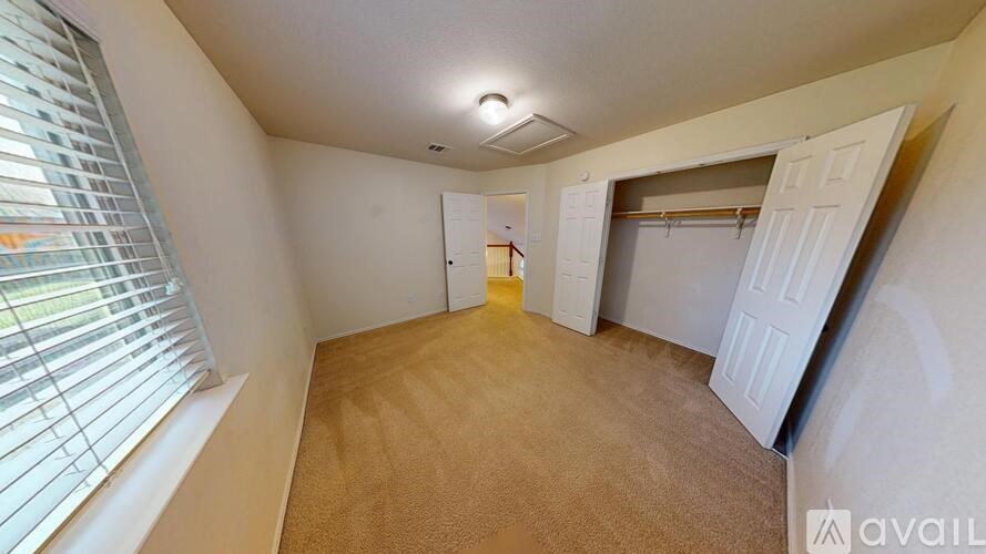 A room with a carpeted floor, a window with blinds, and a door leading to another room.