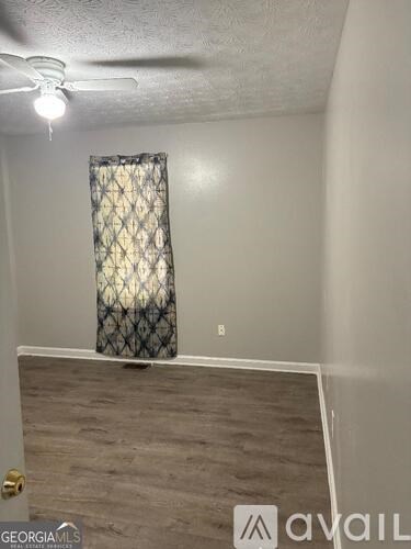 A room with a ceiling fan and a window with a patterned curtain.