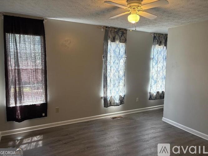 A room with a ceiling fan and three windows with curtains.