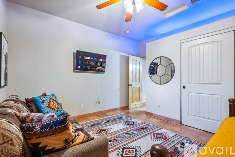 A living room with a couch, a rug, a ceiling fan, and a TV mounted on the wall.