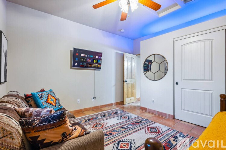 A living room with a couch, a rug, a ceiling fan, and a TV mounted on the wall.