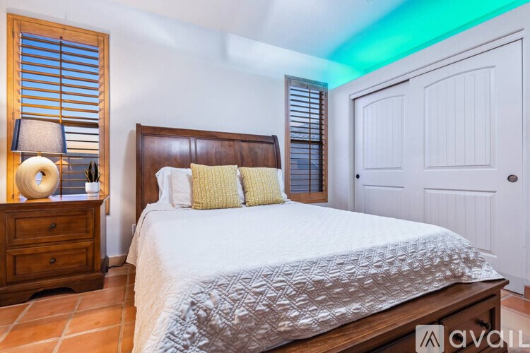 A bedroom with a large bed, a wooden nightstand with a lamp, and a door.