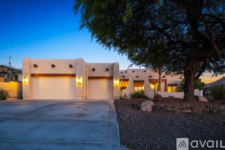 A modern house with a large driveway and a tree in front.