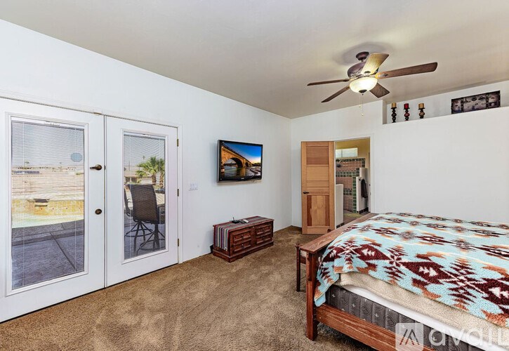 A bedroom with a bed, a ceiling fan, and a painting of a beach scene on the wall.
