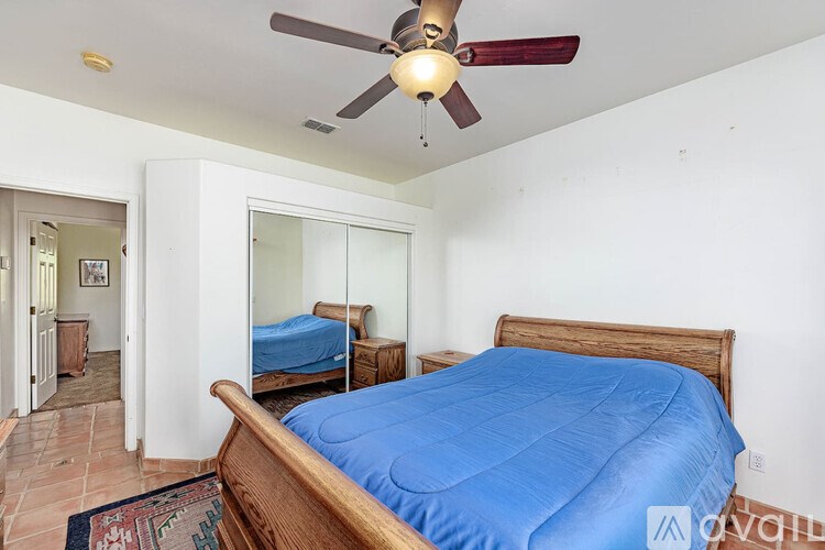 A bedroom with a blue bedspread and a ceiling fan.