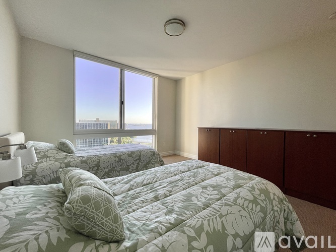 A bedroom with two beds and a large window overlooking a cityscape.