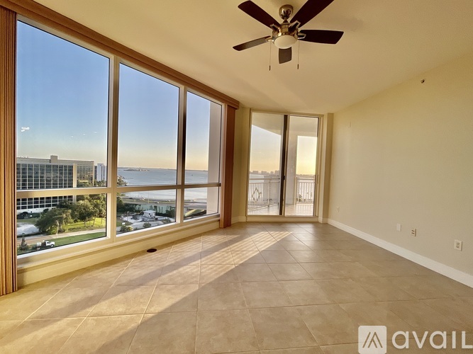 A spacious room with a ceiling fan and large windows overlooking a cityscape.