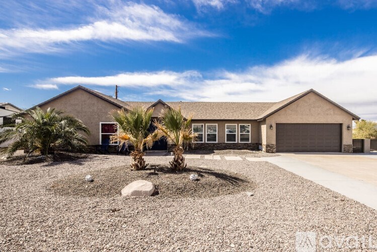 A house with a gravel driveway and two palm trees in front.