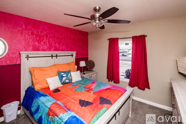 A bedroom with a bed, a ceiling fan, and a window with red curtains.