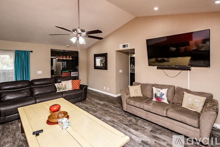 A living room with a black leather couch, a wooden coffee table, and a flat screen TV mounted on the wall.