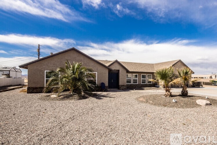 A house with a gravel driveway and two palm trees in front.
