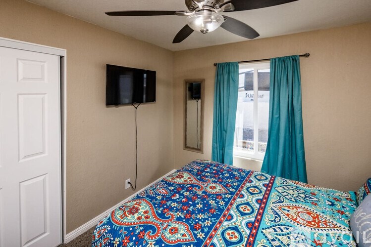 A bedroom with a bed, a ceiling fan, and a flat screen TV mounted on the wall.