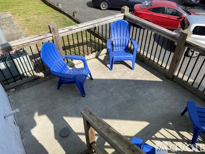 Two blue chairs on a patio with a red car in the background.
