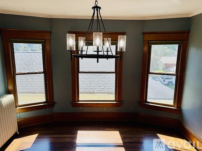 A chandelier hangs over a wooden table in a room with two windows.