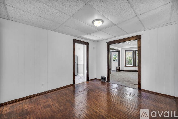 A room with wooden floors and white walls, with a doorway leading to another room.