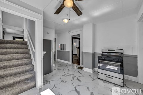 A living room with a grey carpet and a white ceiling fan.