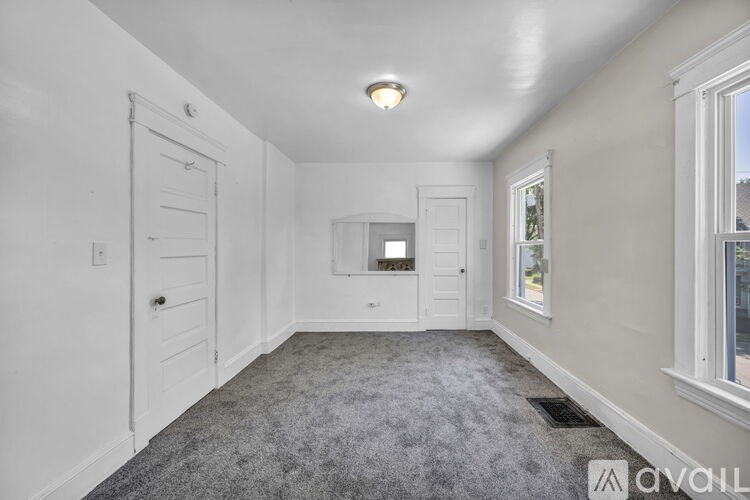 A room with a carpeted floor, a window, and a door.