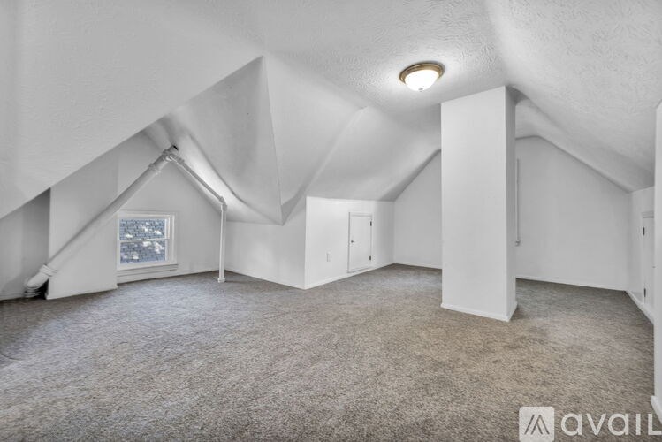 A spacious attic room with a window and carpeted floor.