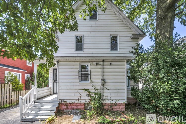 A white house with a porch and a tree in front.