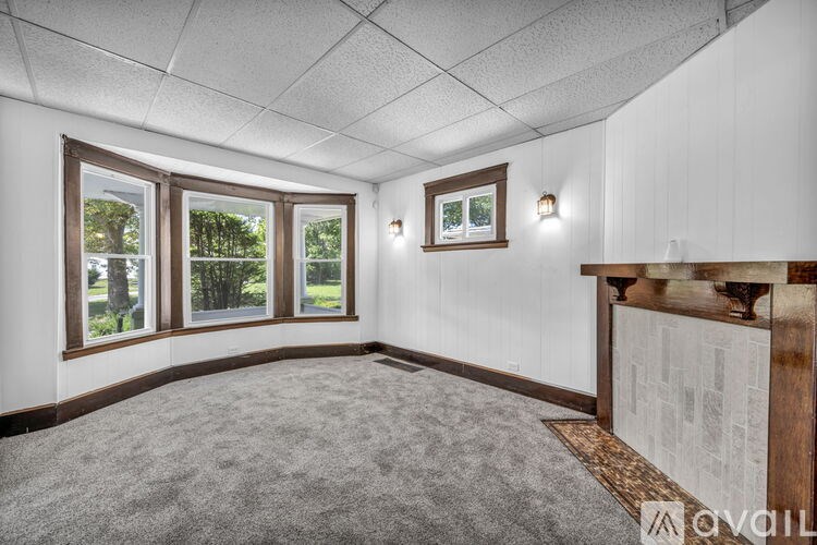 A room with a carpeted floor, a window with a view of trees, and a picture frame on the wall.