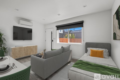 A modern bedroom with a grey couch, a bed, and a television.