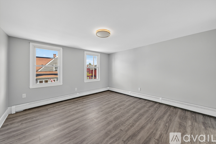 A spacious room with wooden flooring and two windows.