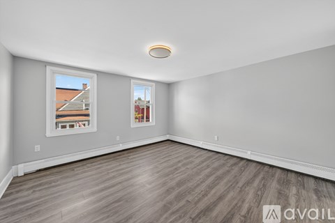 A spacious room with wooden flooring and two windows.