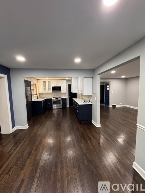 A spacious room with dark wood flooring and a kitchen area in the background.