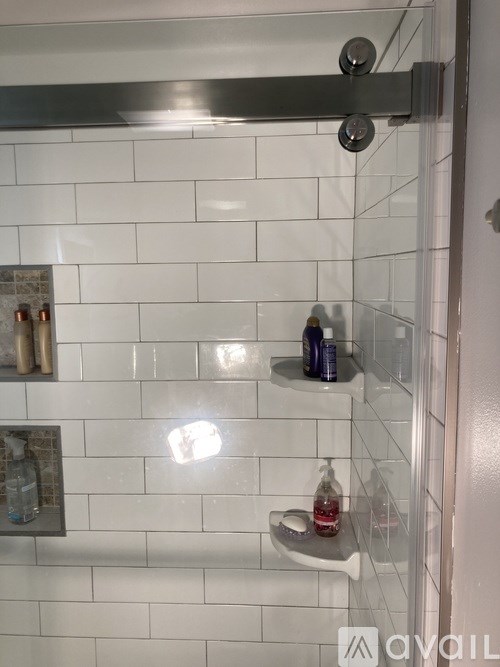 A shower area with a glass door and a white tiled wall.