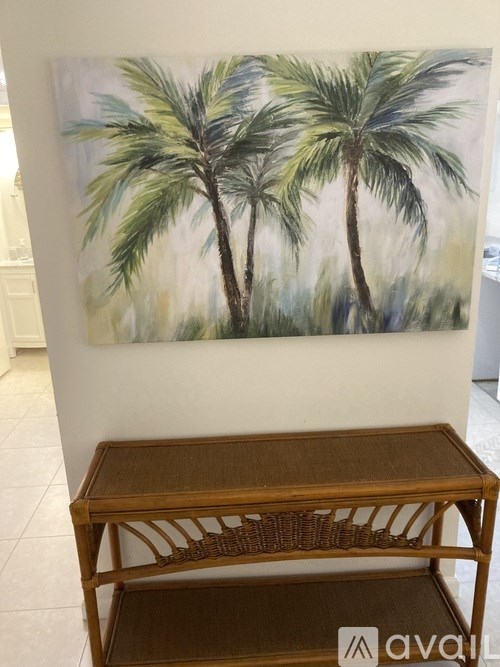 A painting of two palm trees hangs on a wall above a wooden table.