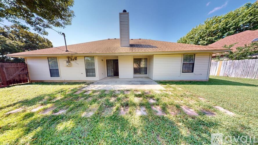 A house with a brown roof and a white exterior is surrounded by a green lawn.