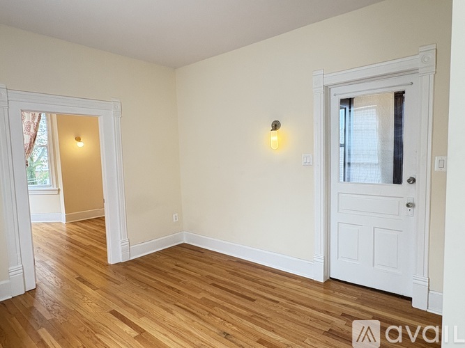 A room with wooden floors and white walls, with a door on the right and a window on the left.