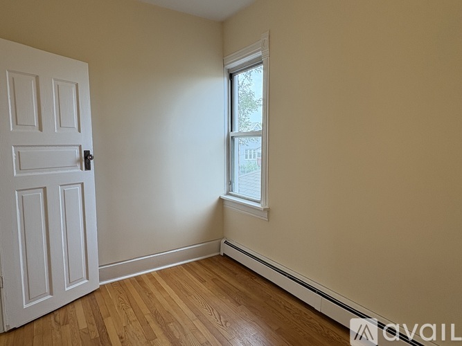 A room with a white door and a window with a view of trees outside.