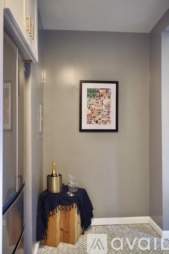 A framed poster of Adams Morgan is hanging on the wall above a table with a bottle and glasses on it.