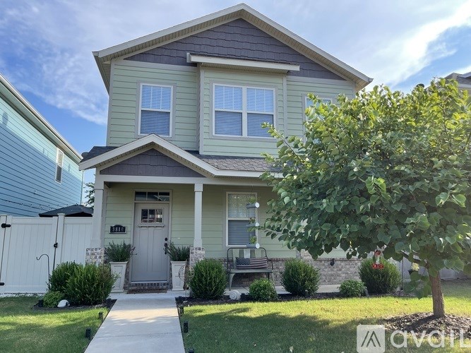 A two-story house with a front porch and a tree in front.