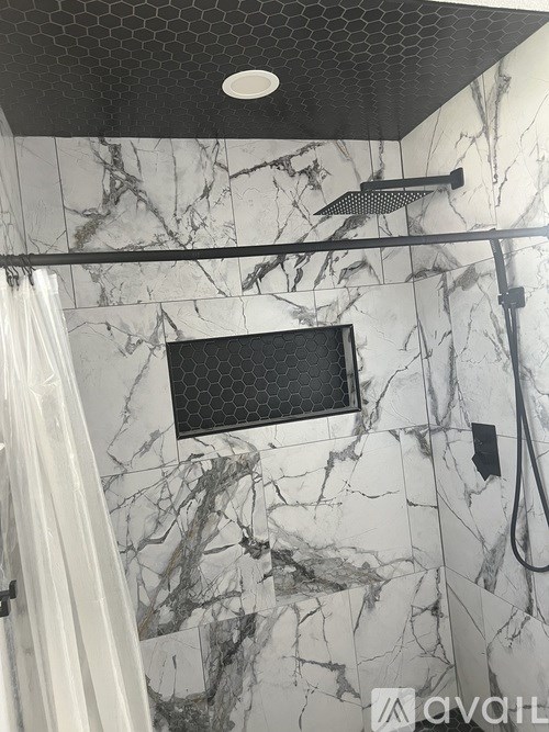 A bathroom with a marble wall and a black shower head.