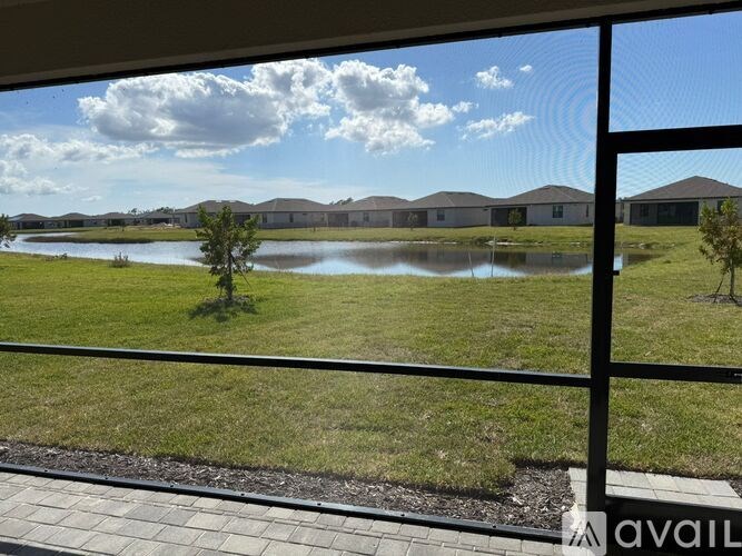 A view from a balcony looking out at a grassy field with a pond and houses in the distance.